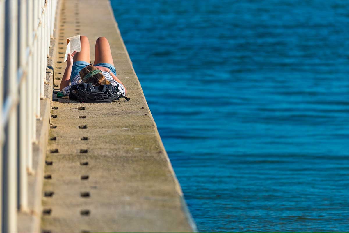 relaxing and reading a book on a concrete pier next to a blue sea with small waves in St Kilda, Victoria, Australia